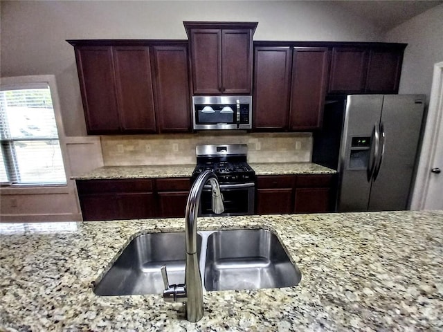 kitchen with light stone countertops, dark brown cabinetry, decorative backsplash, stainless steel appliances, and a sink