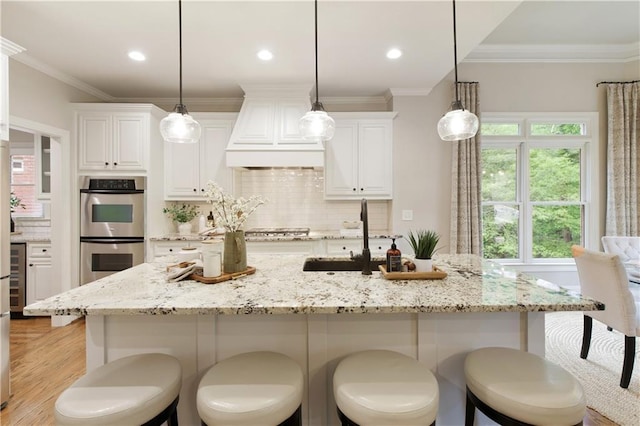 kitchen with backsplash, appliances with stainless steel finishes, a sink, premium range hood, and light wood-style flooring