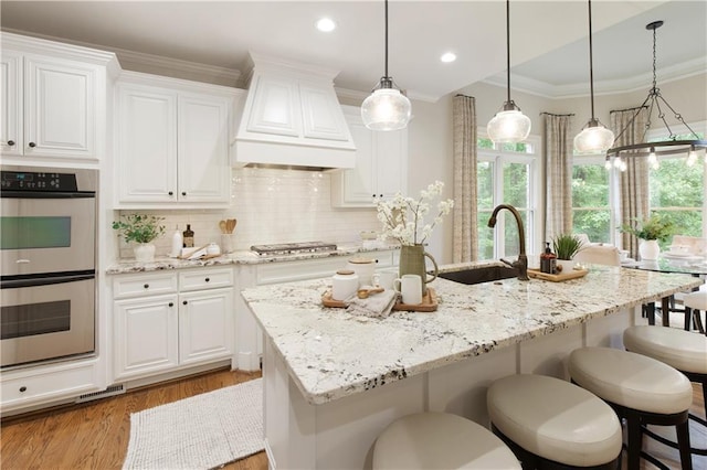 kitchen with light stone countertops, premium range hood, white cabinetry, a sink, and stainless steel appliances