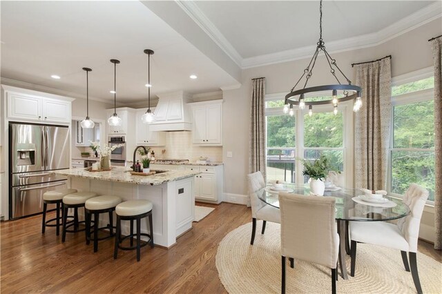 kitchen with appliances with stainless steel finishes, premium range hood, white cabinetry, backsplash, and ornamental molding