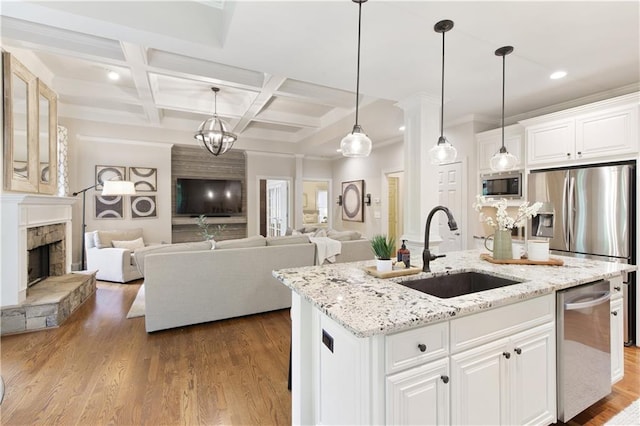 kitchen with a stone fireplace, stainless steel appliances, a sink, coffered ceiling, and white cabinetry
