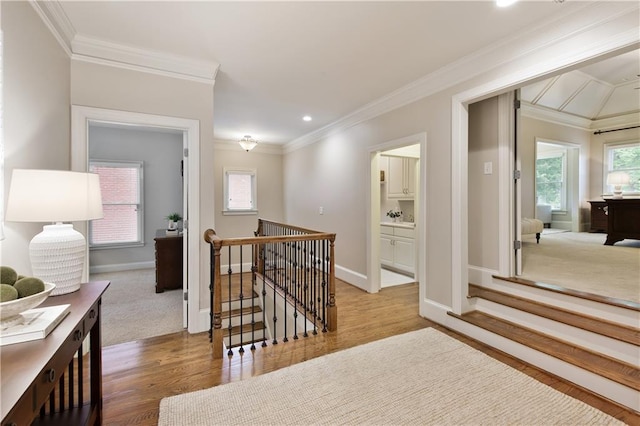 hallway with baseboards, ornamental molding, wood finished floors, and an upstairs landing