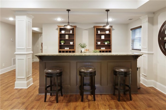 bar featuring decorative light fixtures, ornate columns, baseboards, and light wood-type flooring
