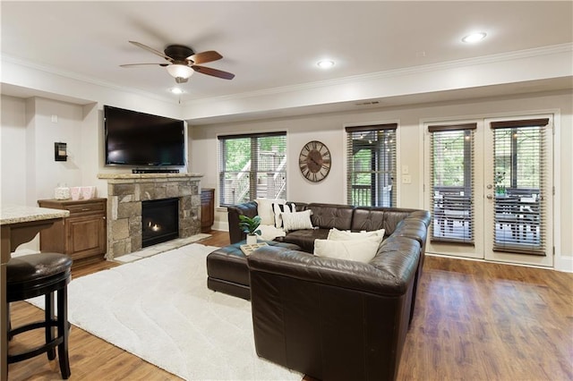 living area with ceiling fan, a stone fireplace, crown molding, wood finished floors, and baseboards
