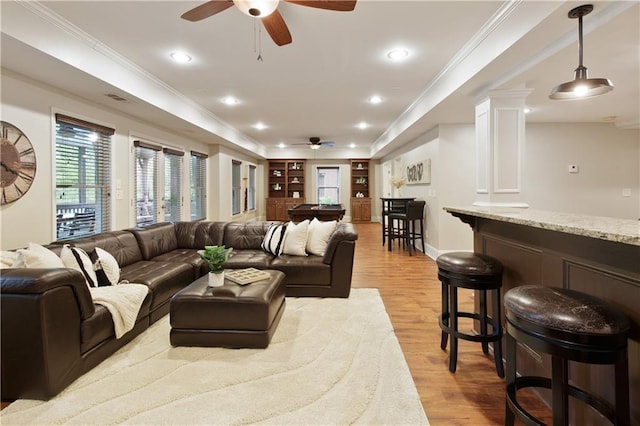 living area with crown molding, a ceiling fan, light wood finished floors, and built in shelves