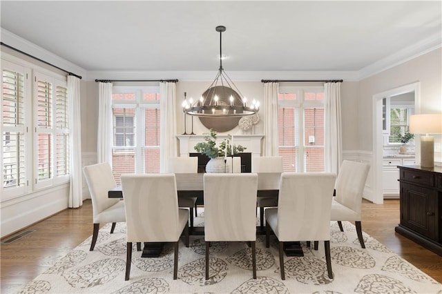 dining room featuring an inviting chandelier, crown molding, wainscoting, visible vents, and wood finished floors