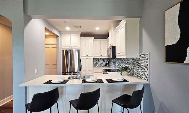 kitchen with a kitchen bar, a peninsula, white cabinetry, stainless steel appliances, and backsplash
