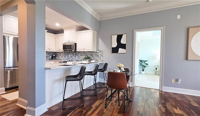 kitchen with backsplash, crown molding, white cabinets, dark wood finished floors, and stainless steel appliances