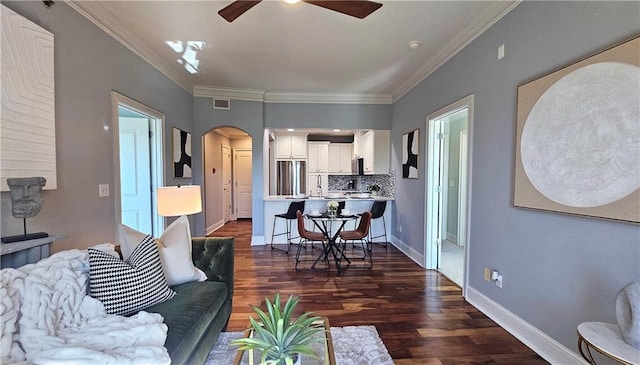 living area featuring baseboards, crown molding, dark wood-type flooring, ceiling fan, and arched walkways