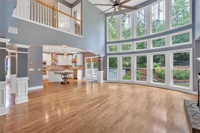 212 Thorncliff Way, Acworth, GA 30101 - unfurnished living room featuring ornate columns, a towering ceiling, ceiling fan, arched walkways, and light wood finished floors