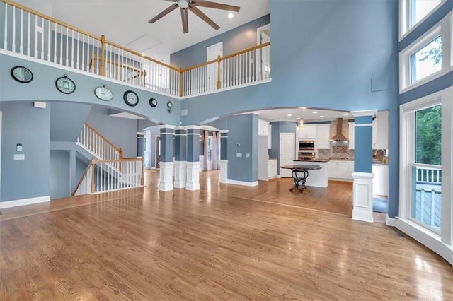 212 Thorncliff Way, Acworth, GA 30101 - unfurnished living room with ceiling fan, a high ceiling, light wood-style flooring, arched walkways, and ornate columns