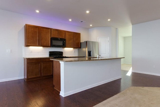 kitchen featuring light stone counters, a center island with sink, black appliances, tasteful backsplash, and dark hardwood / wood-style flooring