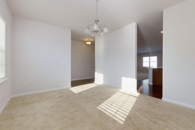 carpeted empty room with an inviting chandelier