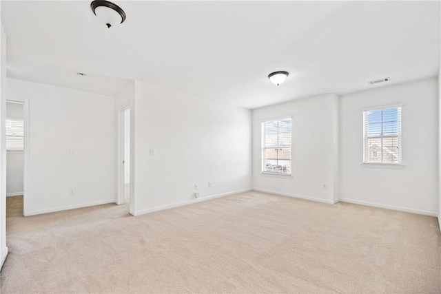 spare room with light carpet, visible vents, and baseboards
