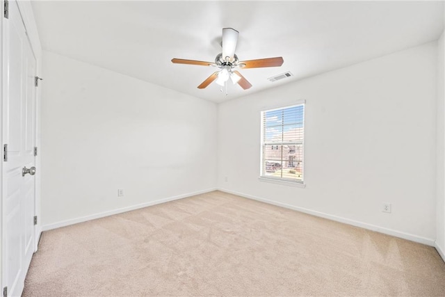 spare room with light colored carpet, ceiling fan, visible vents, and baseboards