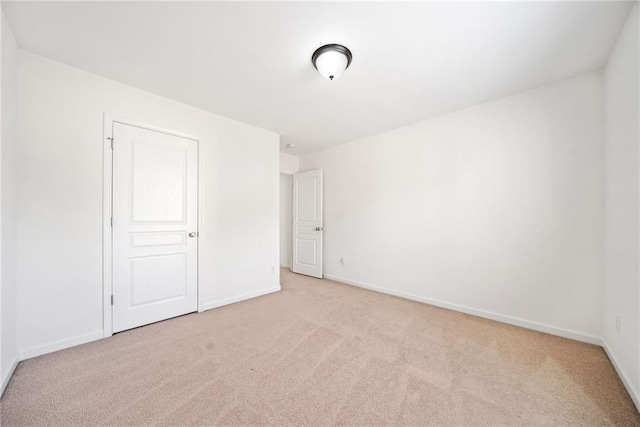 spare room featuring light colored carpet and baseboards