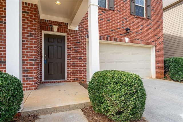 view of exterior entry with a garage, driveway, and brick siding