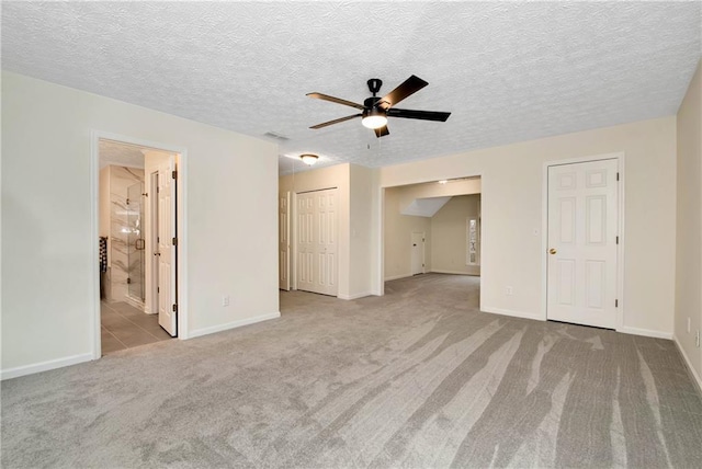 unfurnished bedroom featuring ceiling fan, light colored carpet, connected bathroom, and a textured ceiling