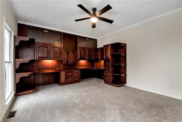 unfurnished office featuring built in desk, ornamental molding, ceiling fan, light carpet, and a textured ceiling