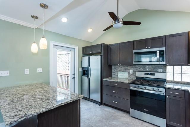 kitchen with decorative light fixtures, lofted ceiling, light stone counters, decorative backsplash, and appliances with stainless steel finishes