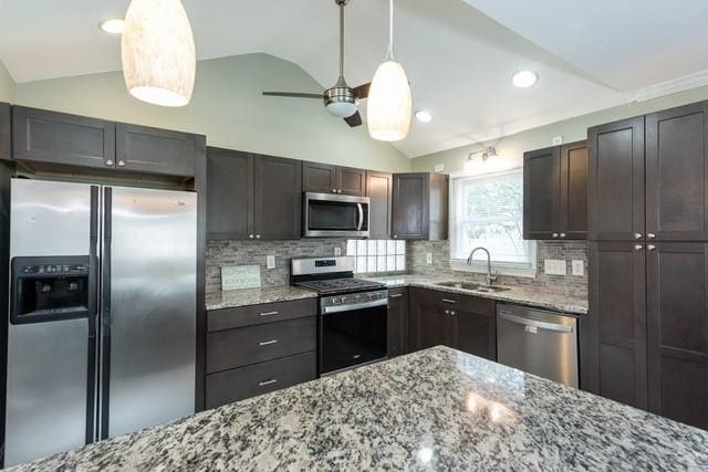 kitchen featuring appliances with stainless steel finishes, light stone countertops, lofted ceiling, and a sink