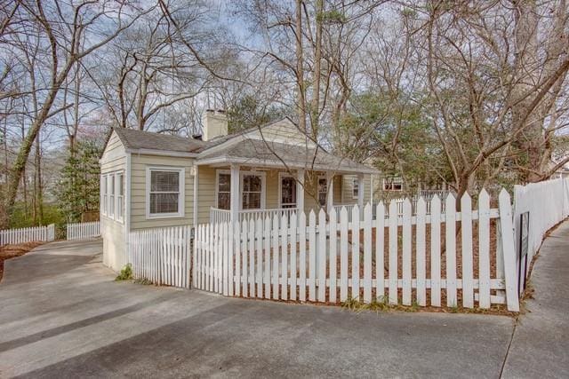 bungalow featuring driveway, covered porch, a fenced front yard, and a chimney