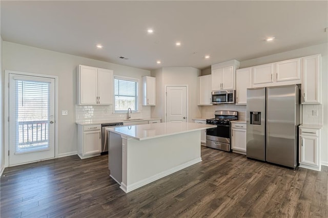 kitchen with appliances with stainless steel finishes, dark hardwood / wood-style flooring, sink, white cabinets, and a center island