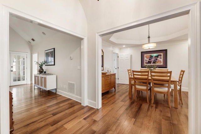 dining space featuring hardwood / wood-style flooring, lofted ceiling, and a raised ceiling