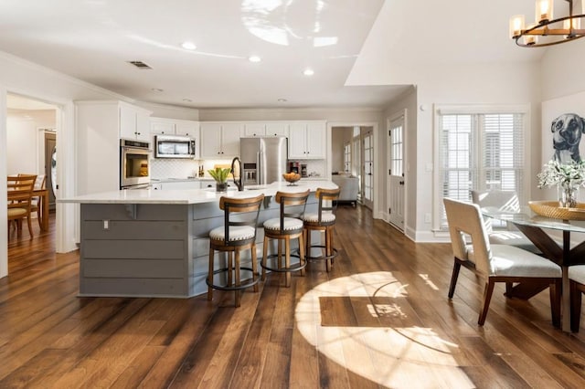 kitchen with appliances with stainless steel finishes, white cabinets, backsplash, a large island, and a notable chandelier