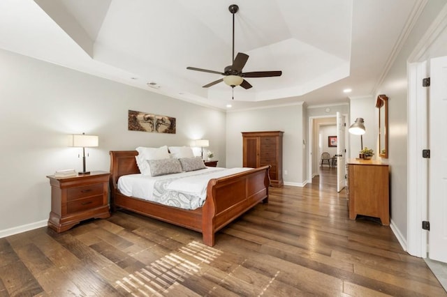 bedroom featuring dark hardwood / wood-style flooring, a tray ceiling, crown molding, and ceiling fan