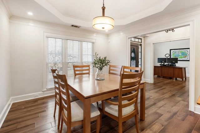 dining space featuring a raised ceiling, ornamental molding, and dark wood-type flooring