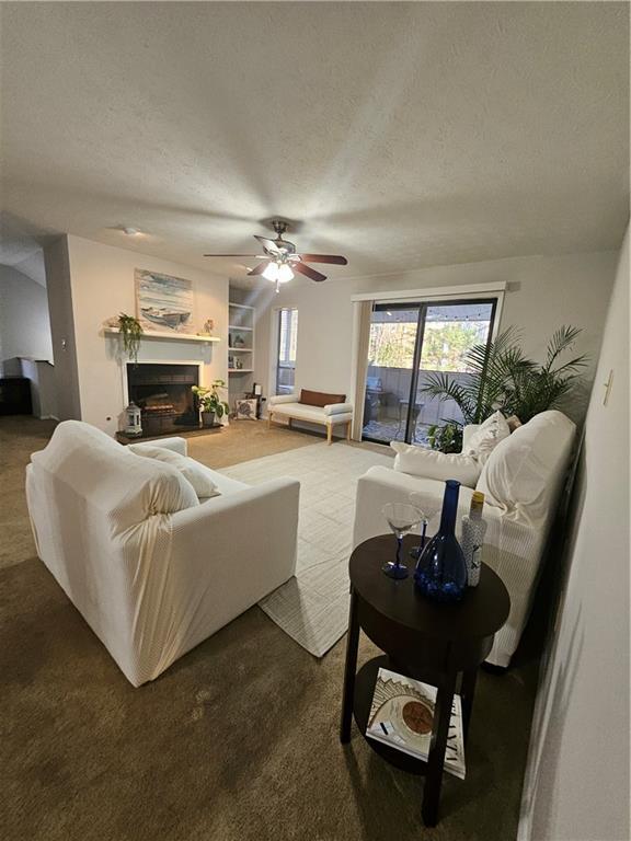 living area with built in shelves, a textured ceiling, a fireplace with raised hearth, and a ceiling fan