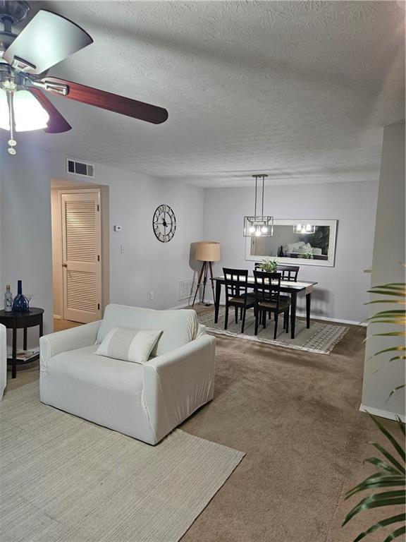 carpeted living room with visible vents, a textured ceiling, and ceiling fan