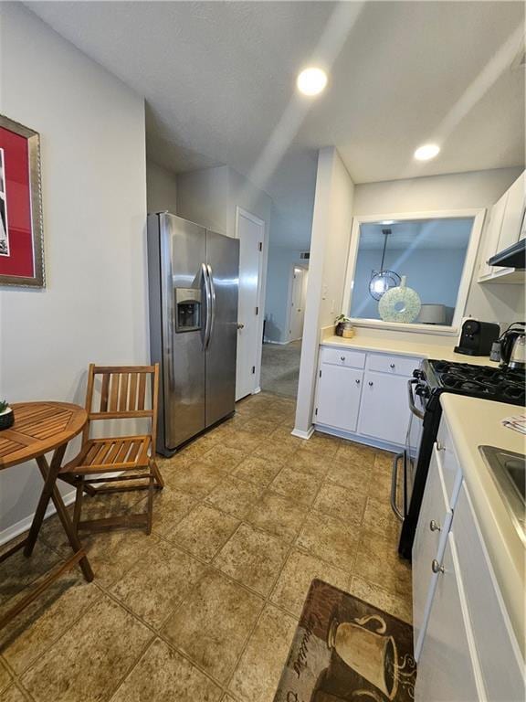 kitchen with baseboards, black gas stove, light countertops, white cabinetry, and stainless steel fridge