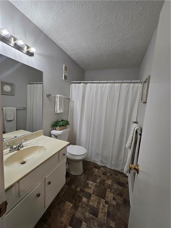 full bath featuring visible vents, toilet, stone finish flooring, a textured ceiling, and vanity