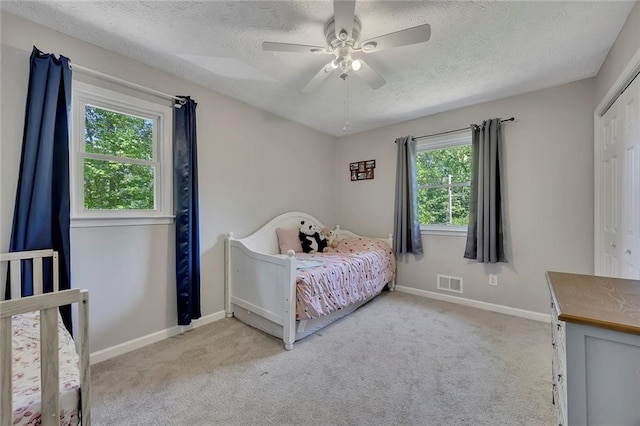 carpeted bedroom with baseboards, a ceiling fan, visible vents, and a textured ceiling