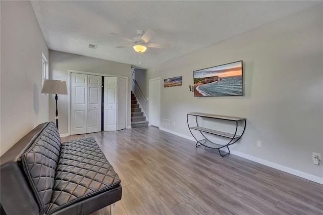 unfurnished room featuring wood finished floors, baseboards, ceiling fan, and stairs
