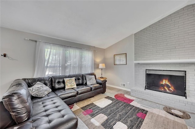 living room featuring wood finished floors, a brick fireplace, visible vents, baseboards, and lofted ceiling