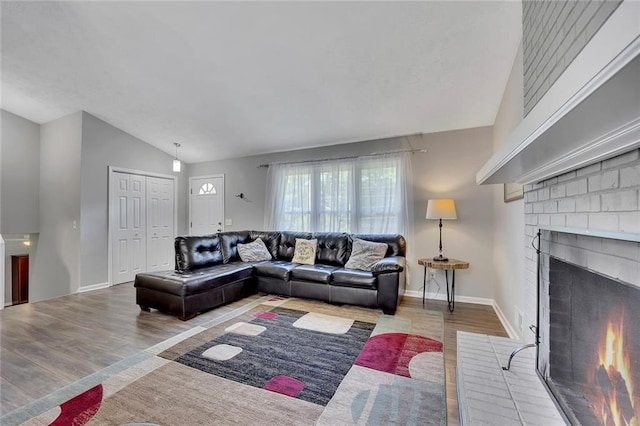 living room with vaulted ceiling, wood finished floors, baseboards, and a brick fireplace