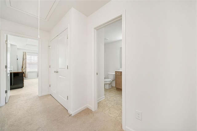 hall featuring light carpet, attic access, and baseboards