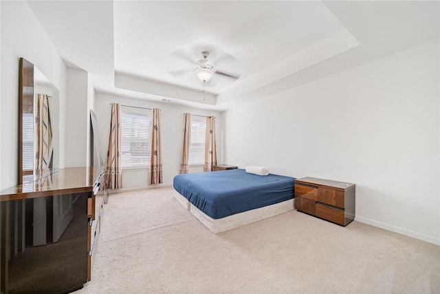 carpeted bedroom with ceiling fan, a tray ceiling, and baseboards