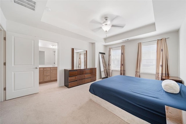 bedroom featuring light carpet, a raised ceiling, visible vents, and ensuite bathroom