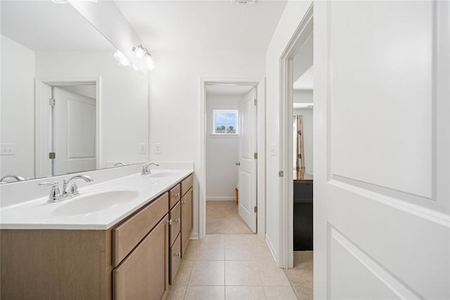 full bath with baseboards, double vanity, a sink, and tile patterned floors