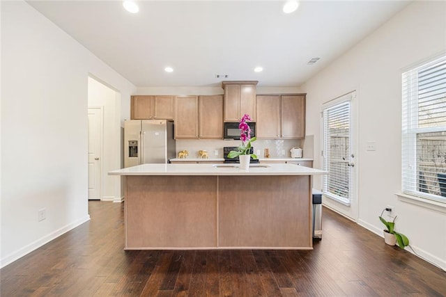 kitchen featuring black microwave, dark wood-type flooring, a kitchen island, light countertops, and stainless steel fridge