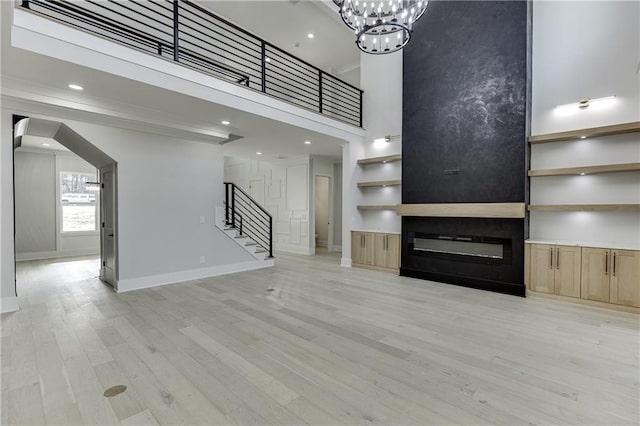 unfurnished living room featuring a towering ceiling, an inviting chandelier, a fireplace, and light wood-type flooring