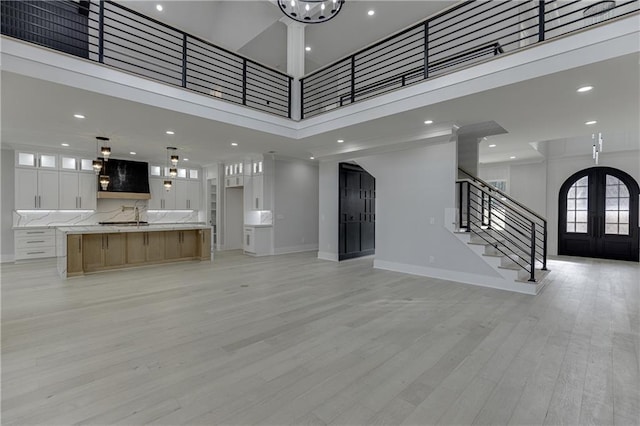 unfurnished living room with sink, a towering ceiling, french doors, and light wood-type flooring