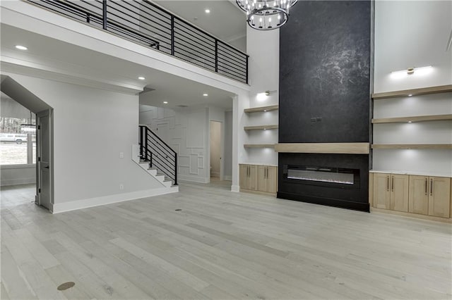 unfurnished living room with ornamental molding, a chandelier, a high ceiling, and light wood-type flooring