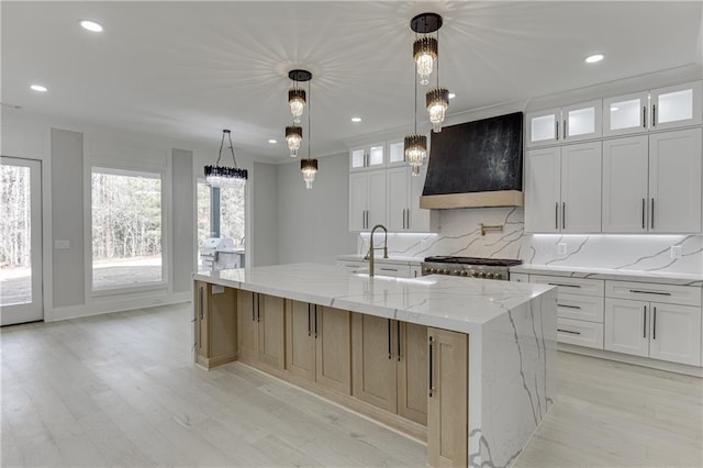 kitchen with a large island, hanging light fixtures, white cabinets, and premium range hood