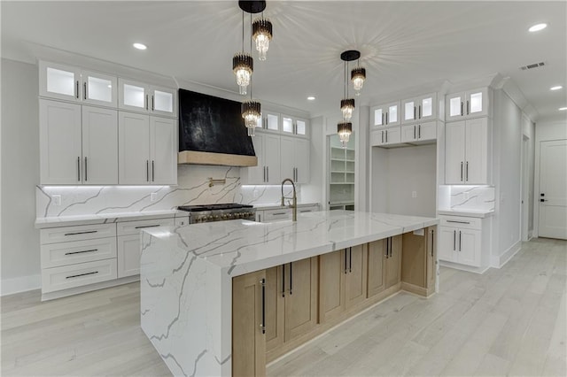 kitchen featuring stove, hanging light fixtures, a spacious island, custom range hood, and white cabinets