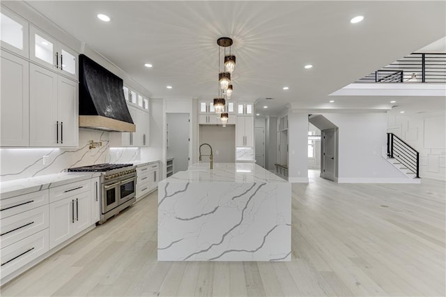 kitchen with white cabinetry, a center island with sink, custom exhaust hood, and range with two ovens